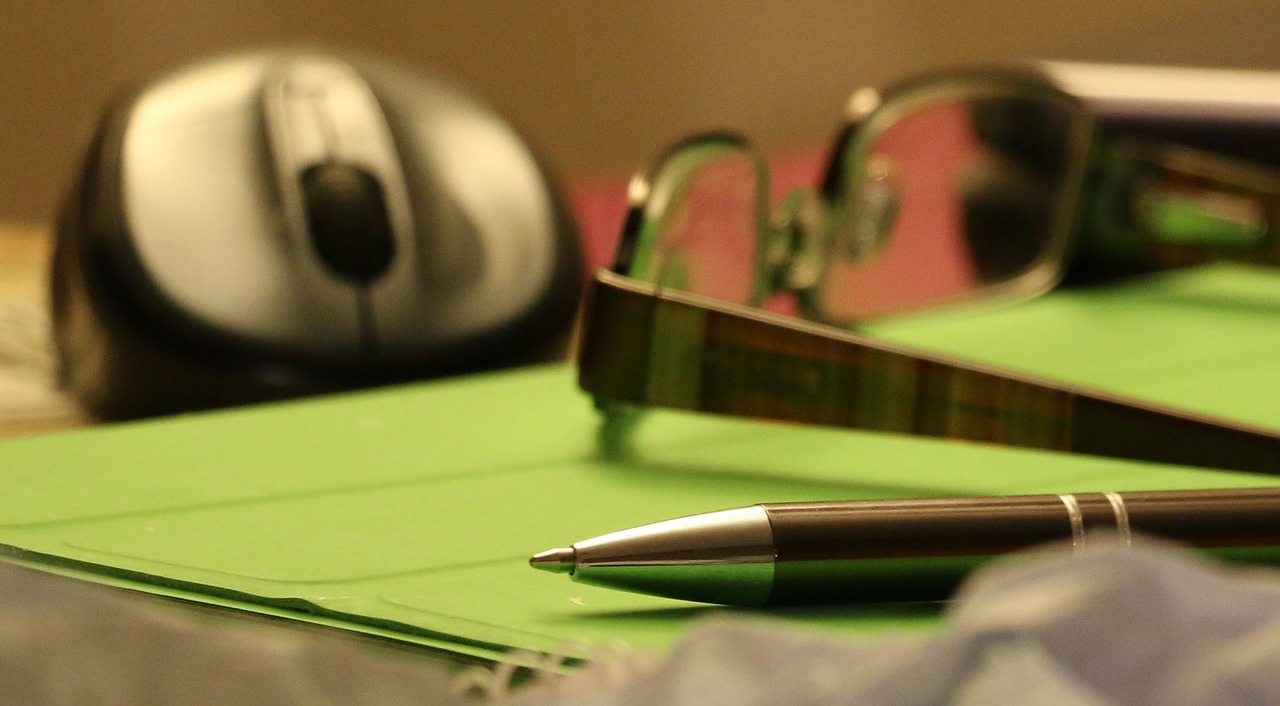 Pen, glasses, and mouse on green notebook